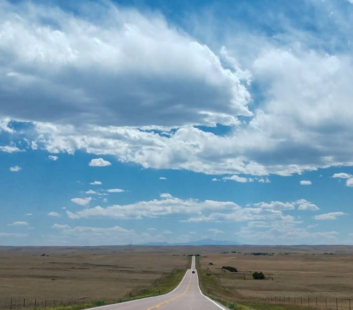 Image of blue sky with clouds and a long road going over the horizon